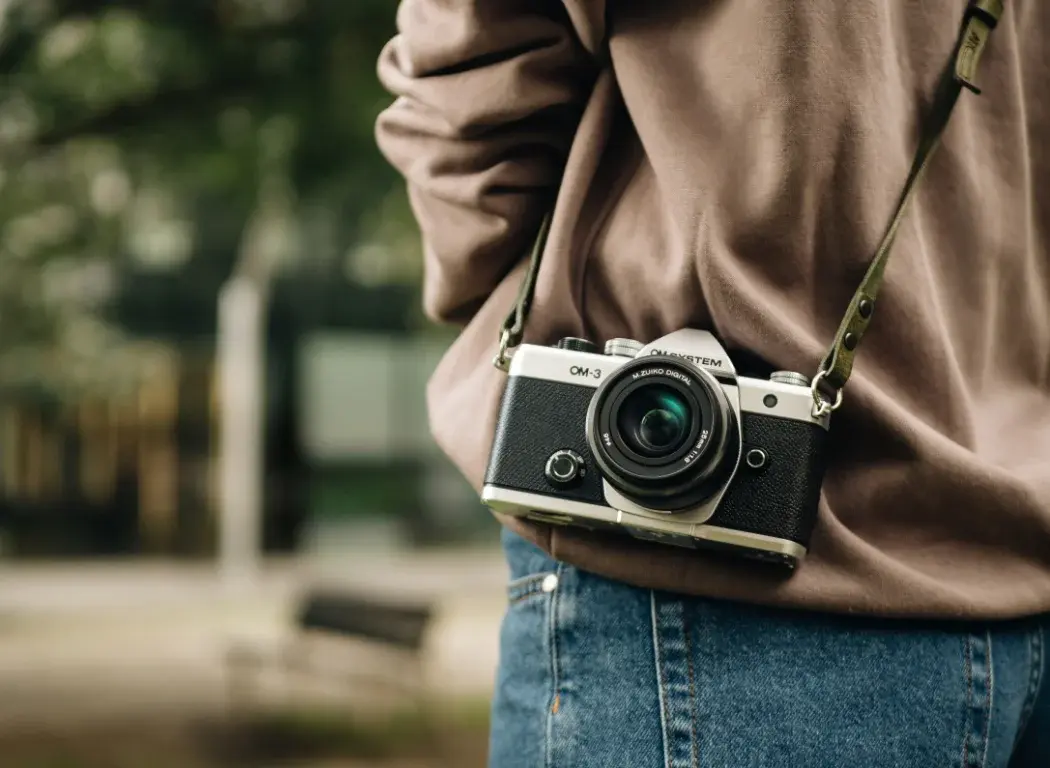 OM SYSTEM OM-3 camera hanging from the neck strap over the should of a person out taking photos.